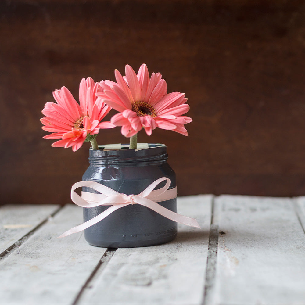 Pink gerbera daisies in a gray mason jar with ribbon.