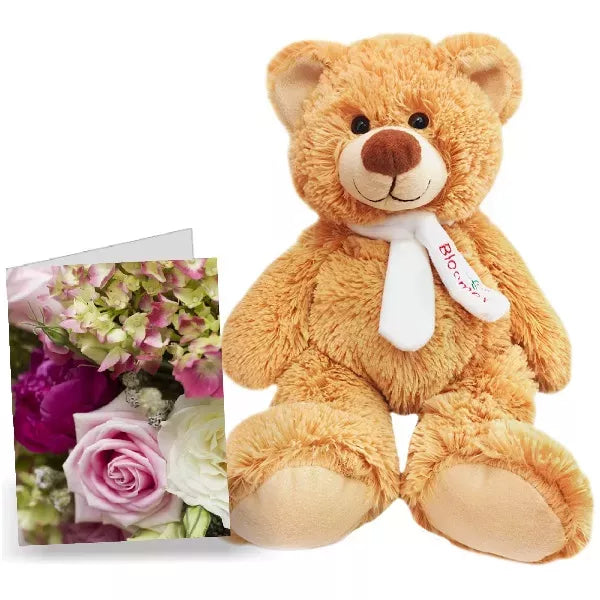 A plush teddy bear with a white bow tie next to a card with flowers.