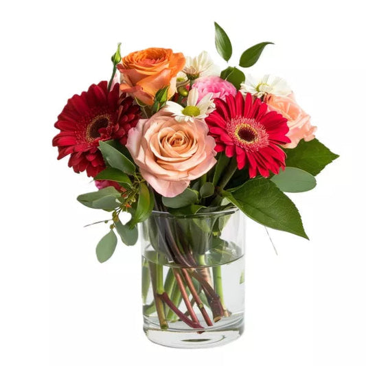 A bouquet of mixed flowers including roses and gerbera daisies in a glass vase.