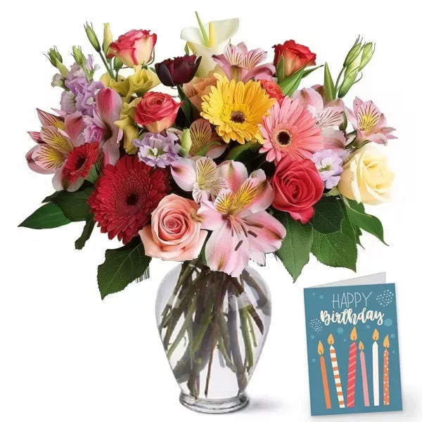 A colorful bouquet of mixed flowers in a clear vase with a 'Happy Birthday' card.