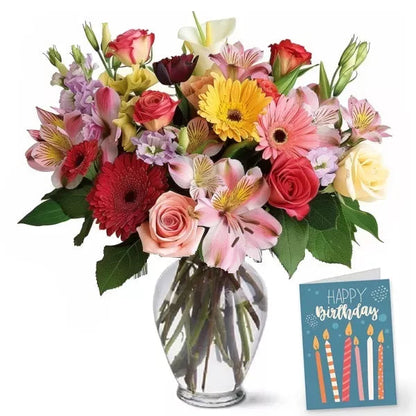 A colorful bouquet of mixed flowers in a clear vase with a 'Happy Birthday' card.