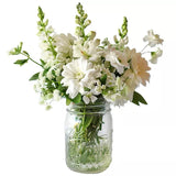 A bouquet of white flowers in a mason jar on a white background.
