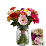 A colorful bouquet of mixed flowers in a mason jar, white background with a small flower card.
