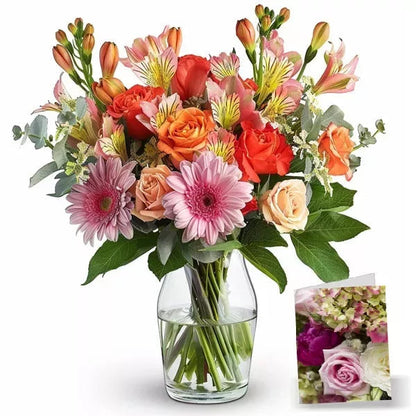 A colorful bouquet of pink gerberas, orange roses, and alstroemeria in a clear glass vase.