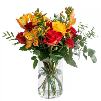 A bouquet of red and yellow roses with yellow alstroemeria in a glass vase on a white background.