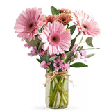 Bouquet of pink gerberas and other flowers in a glass jar tied with a raffia ribbon.