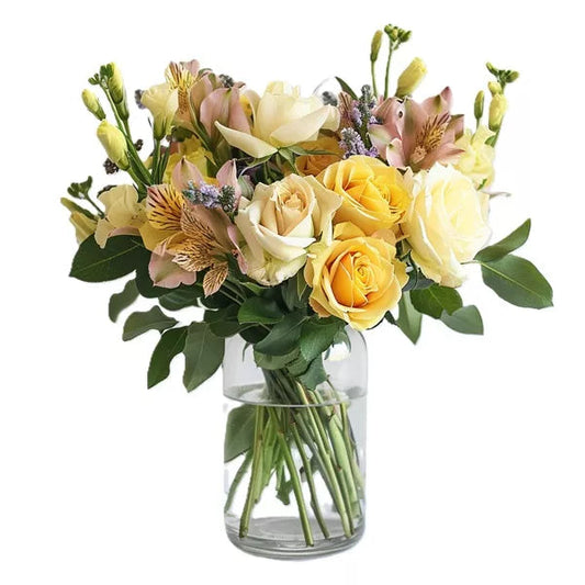 A bouquet of yellow and cream roses with mixed flowers in a glass vase.