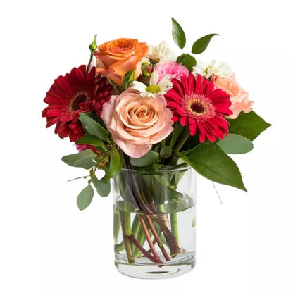 A bouquet of mixed flowers including roses and gerbera daisies in a glass vase.
